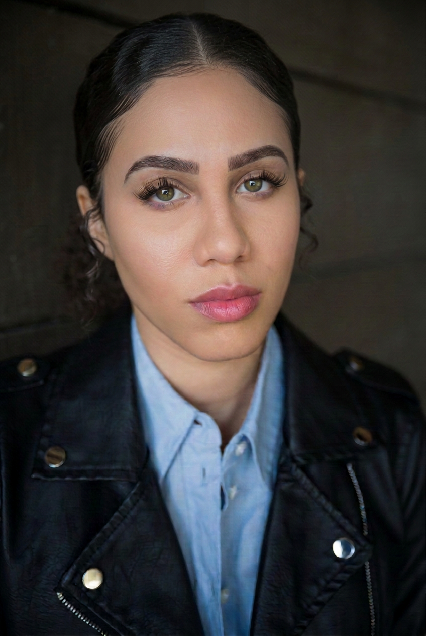 Ashlyn Nichols, theatrical headshot wearing a black leather jacket over a blue shirt.