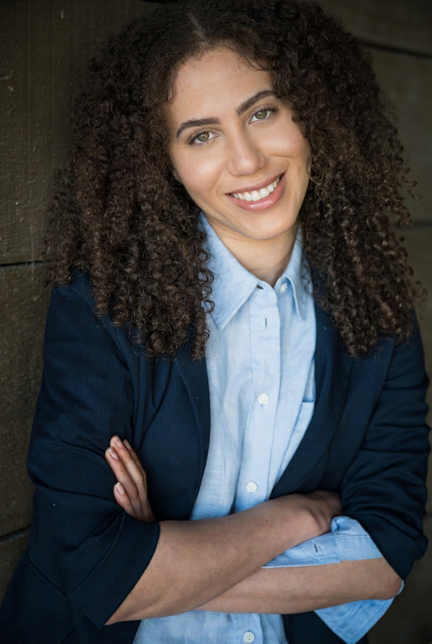 Ashlyn Nichols, natural curls and navy blazer, with a warm direct expression.
